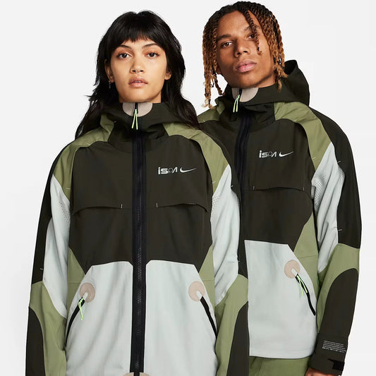 Nike ISPA Jacket in green, black, and grey color-block design, modeled by a man and a woman. Technical outdoor jacket featuring water-resistant shell, full-zip closure, adjustable hood, and performance-ready construction for urban and outdoor wear.