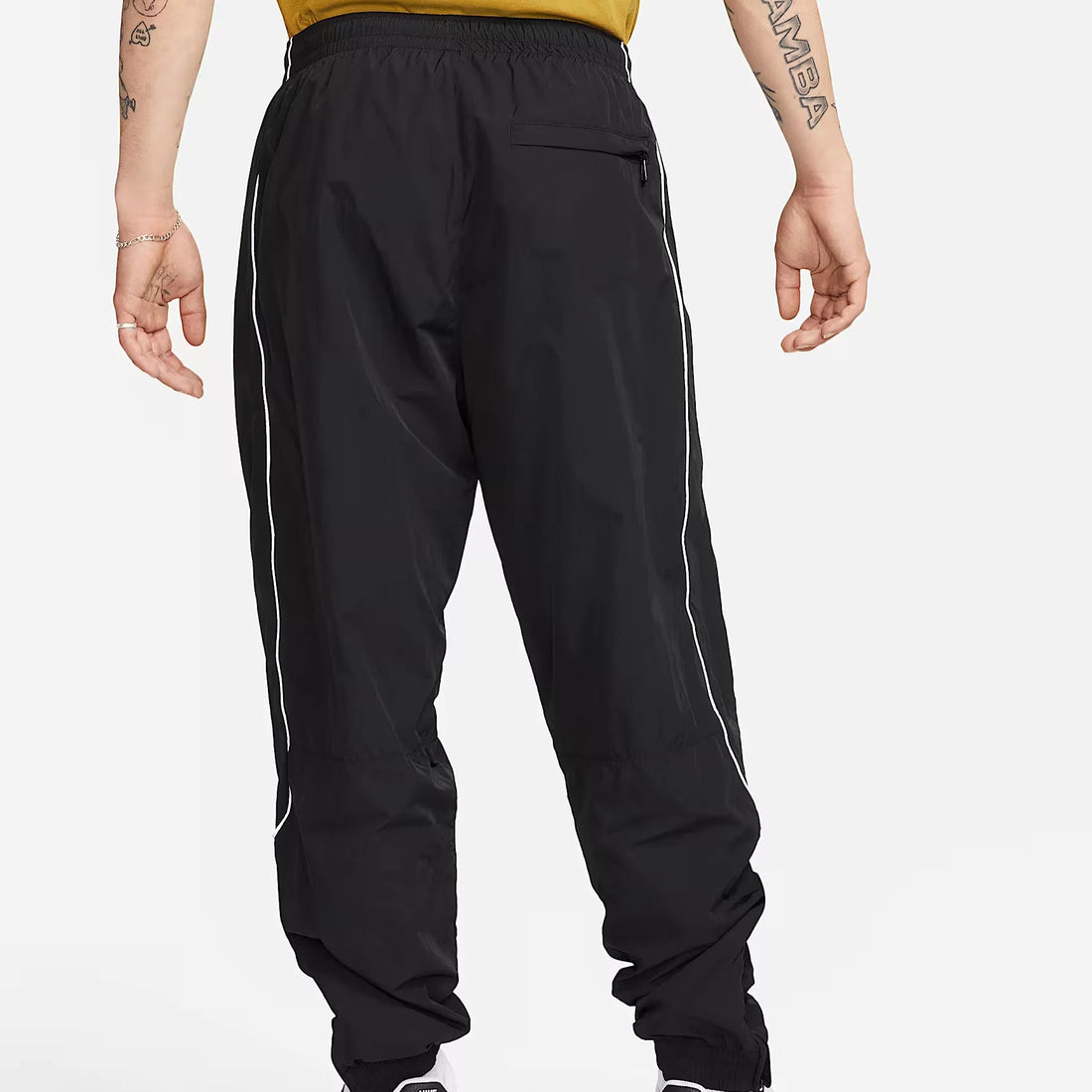 Nike Solo Swoosh Men’s Track Pants in black, front view. Features elastic waistband, side pockets, relaxed fit and reflective piping for modern athletic style.